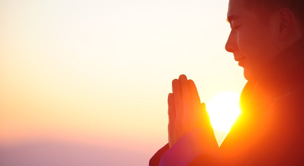 Persona meditando al amanecer con las manos juntas, representando paz mental y emocional.