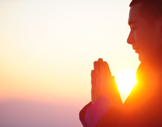 Persona meditando al amanecer con las manos juntas, representando paz mental y emocional.