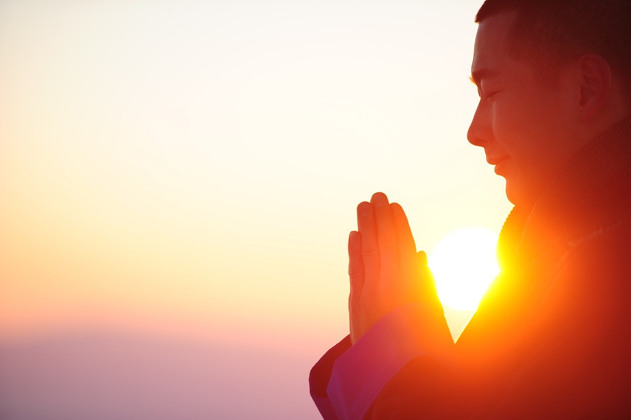 Persona meditando al amanecer con las manos juntas, representando paz mental y emocional.